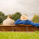 Ett äldre par sitter tillsammans på en parkbänk i grönskan